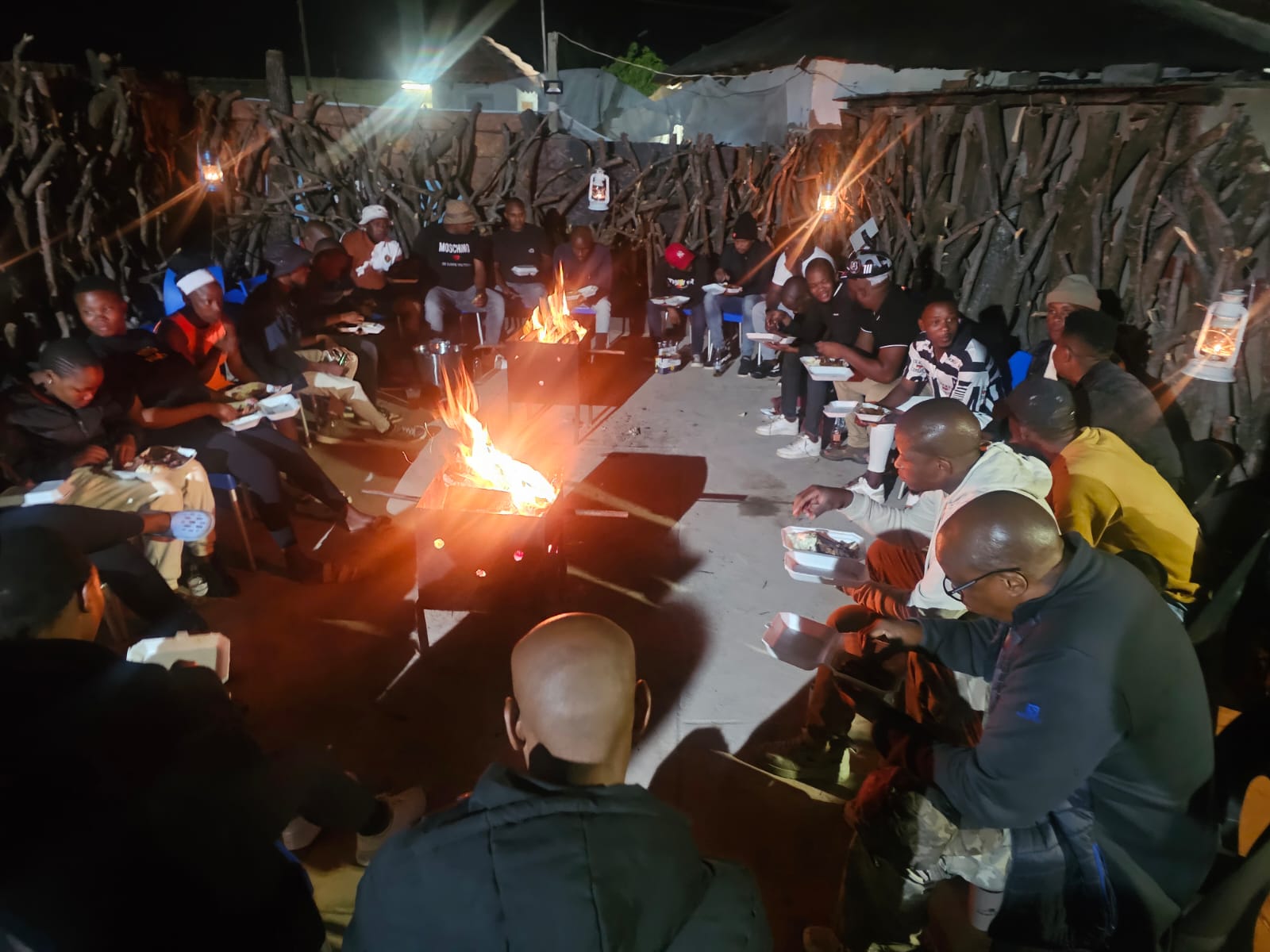 Evening boma dinner with guests gathered around the fire pit eating from takeaway containers